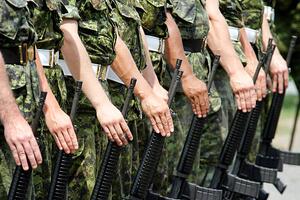 a photograph of soldiers in a row wearing camouflage and each holding a rifle at their side. 