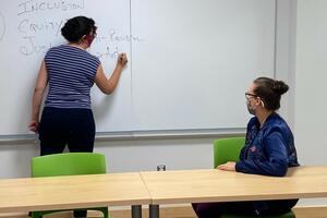 Teacher writing on white board with student sitting in classroom
