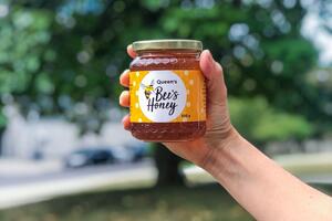 An arm and hand holding a jar of Queen's Bees Honey 