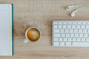A notebook, a coffee, earbuds, and a keyboard on a desk