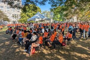 crowd wearing orange, seated and standing outside in benidickson Field