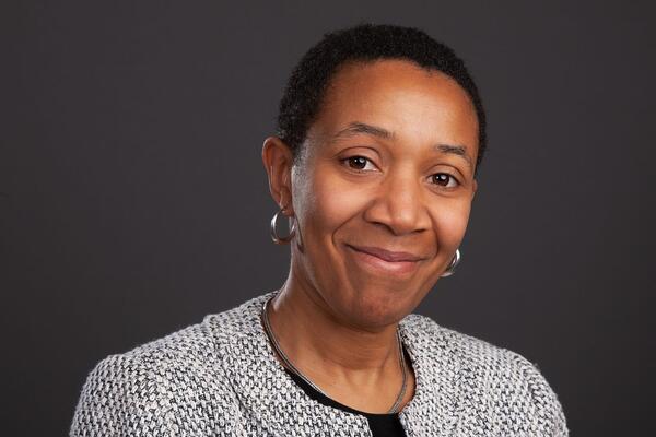 Women in tweed jacket looking at camera, in front of a black background.