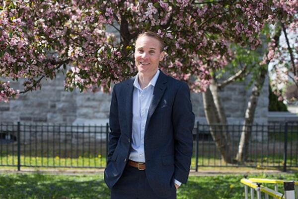 Man with short brown hair in a white collared shirt standing in front of a flowering tree.