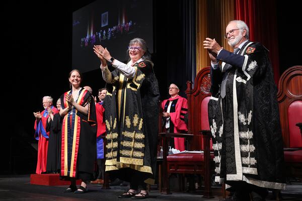 Five people on a stage in academic regalia clapping