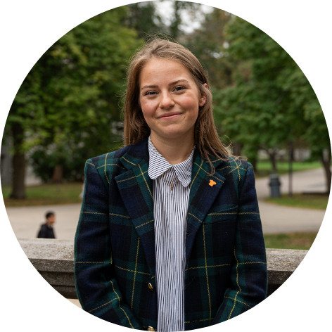 Young woman with long hair, wearing a plaid green suit jacket, smiling at camera.