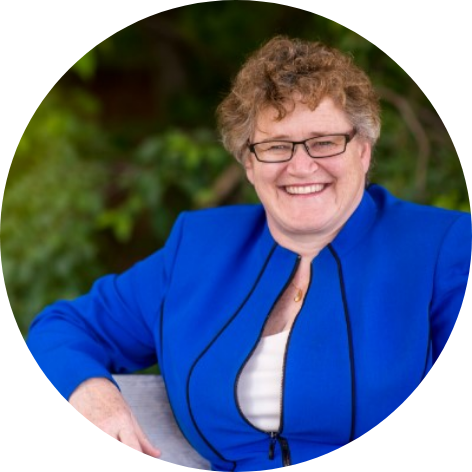 Woman with short hair wearing a bright blue suit, sitting on a bench with her arm resting on the top of it, smiling at the camera.