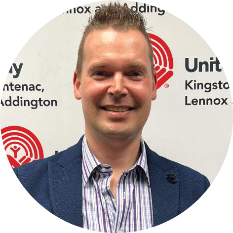 Man with spiky blond hair, wearing a navy suit and stripped button up, smiling at the camera.