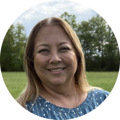 Woman with long light brown hair, wearing a light blue blouse, smiling at the camera.