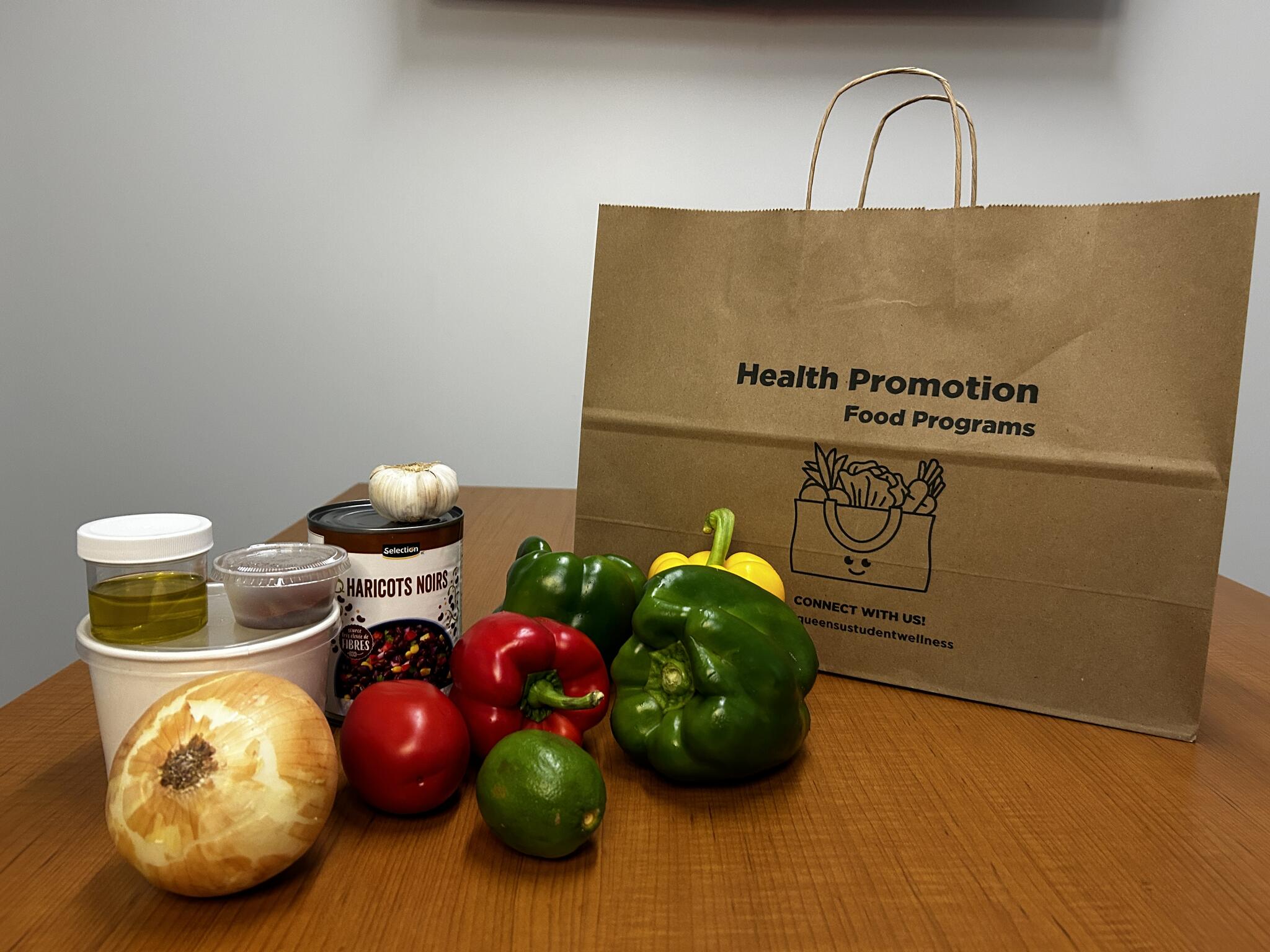 Paper bag with green, red, and yellow peppers, an onion, and various spice containers on a wood table