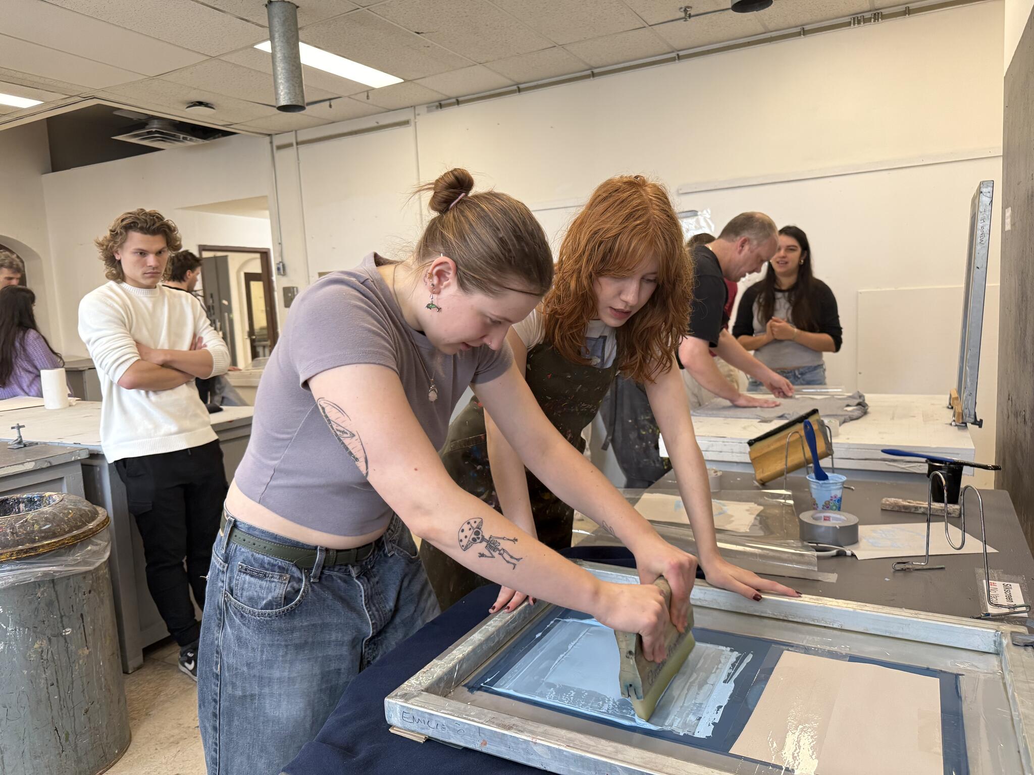 A student in a purple shirt using a screen to press an image on a t-shirt