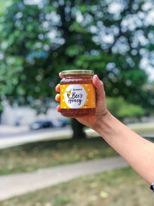 An arm and hand holding a jar of Queen's Bees Honey