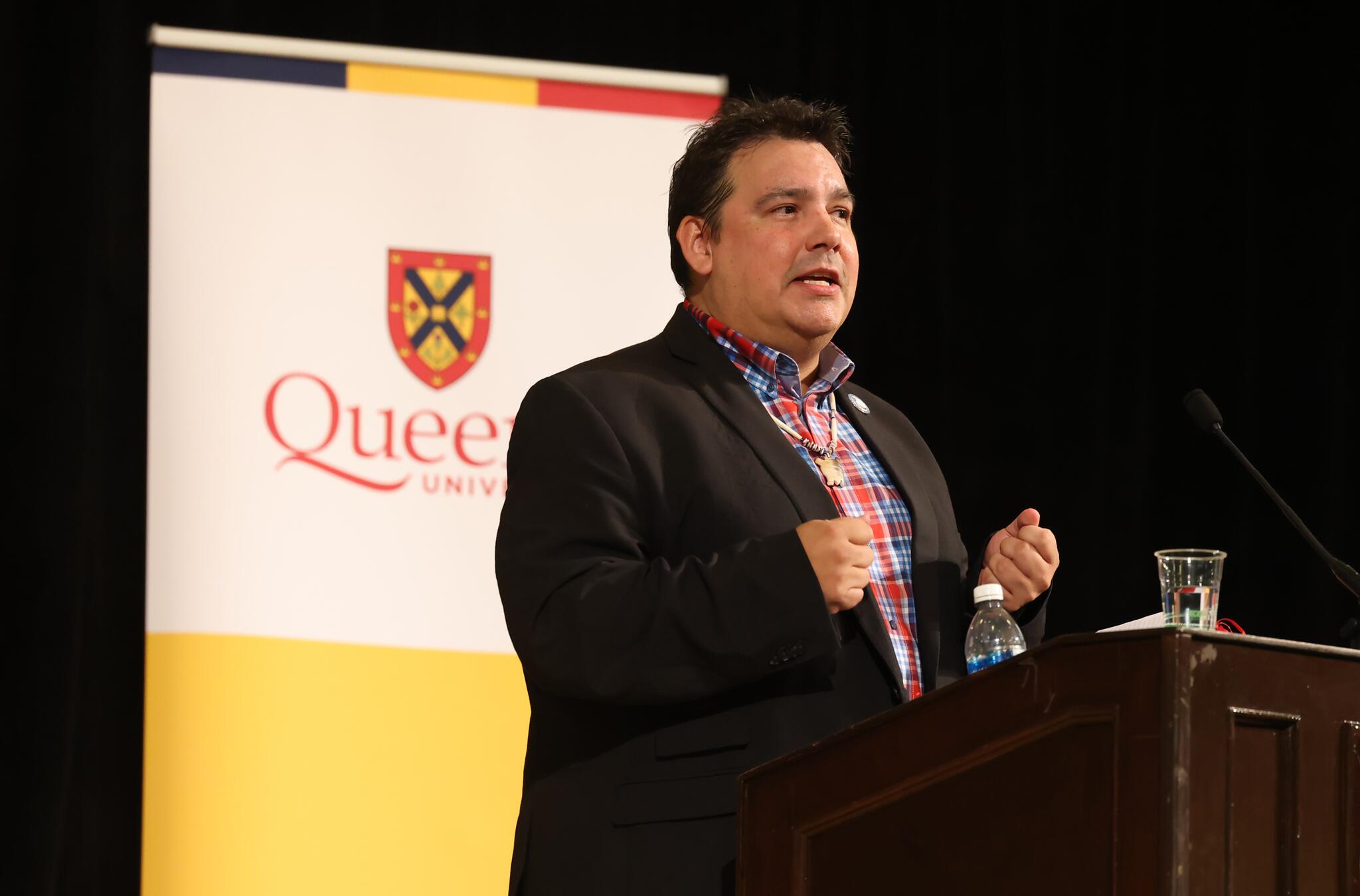 Man with black hair in suit speaking behind wooden podium.