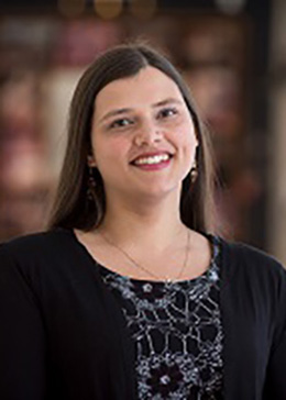 Woman with long brown hair wearing a black cardigan smiling with her head tilted to the left.