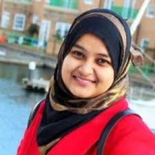 Woman wearing red blazer and dual-ton hijab (black and gold) smiling in front of river.