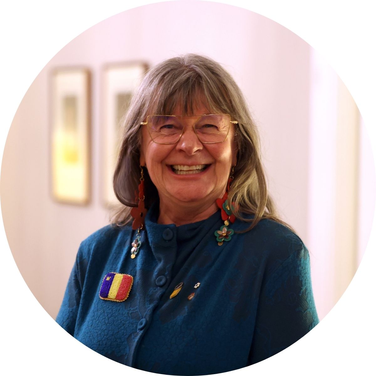 Woman with white hair, wearing long dangling earrings and wide square glasses, smiling.
