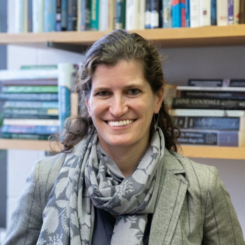 Woman with curly hair pulled back into an updo, wearing a scarf and blazer, looking at the camera.