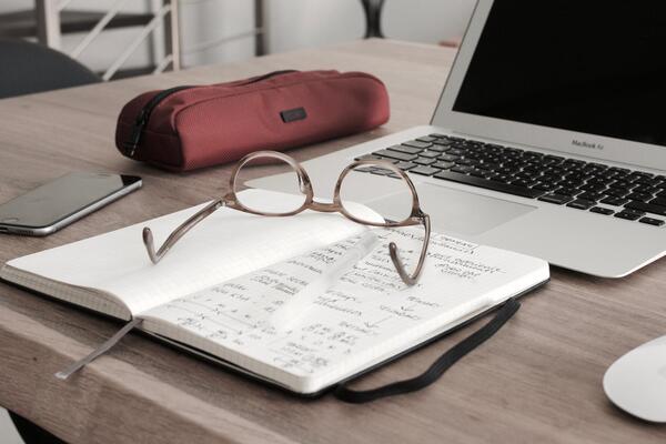 Table top with an open book, laptop, phone and glasses
