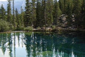 A clear lake with evergreen trees behind it and mountains behind that. 
