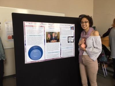 A person smiling in front of a poster