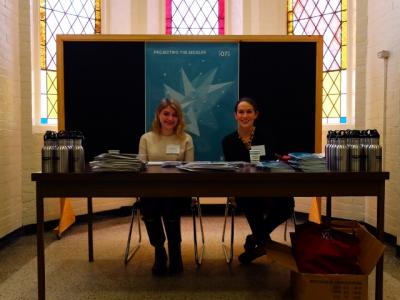 Two people smiling in front of a poster