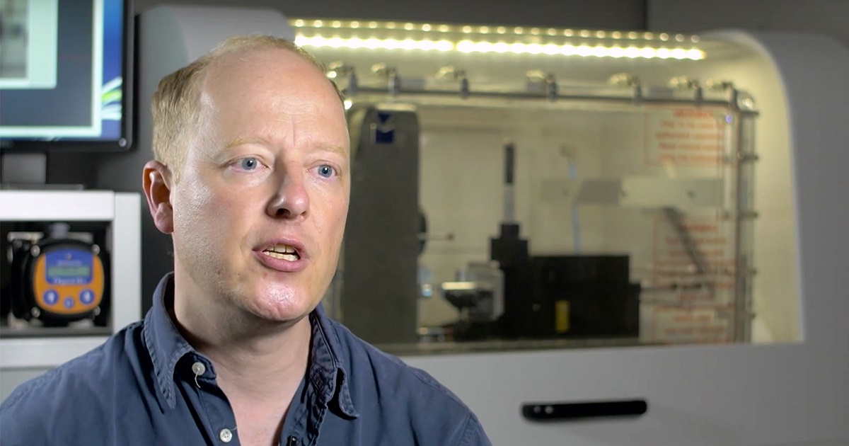 Mark Daymond speaking in front of laboratory equipment.