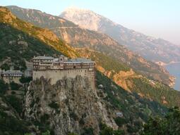 a Monastery on a cliff against a background of mountains and the ocean