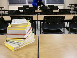 Woman sitting in front of chalk board with books stacked on a desk