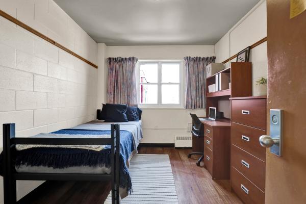 Single room in Jean Royce Hall. Room features a single bed, desk and chair, closet and chest of drawers. 