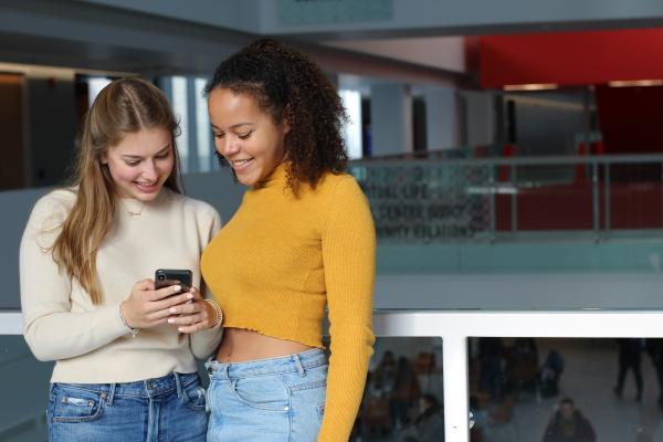 Two students standing together, smiling while looking at a phone. 