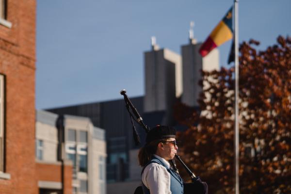 Bagpiper plays in front of a Queen's flag