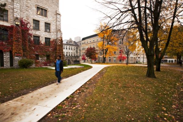 Fall trees by a path between limestone buildings on Queen's campus