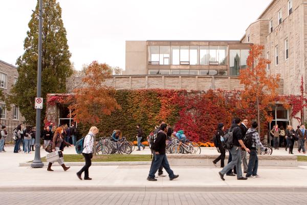 Students walk by a campus building with red fall foliage