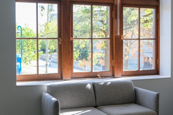 A couch by a large, three-framed window looks out to greenery. Sunlight filters inside.