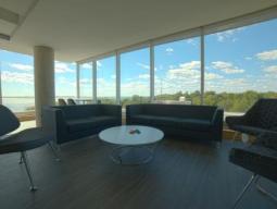 Common room in the summer accommodations. The rooms features couches and chairs in the room with the Kingston landscape visible through the windows. 