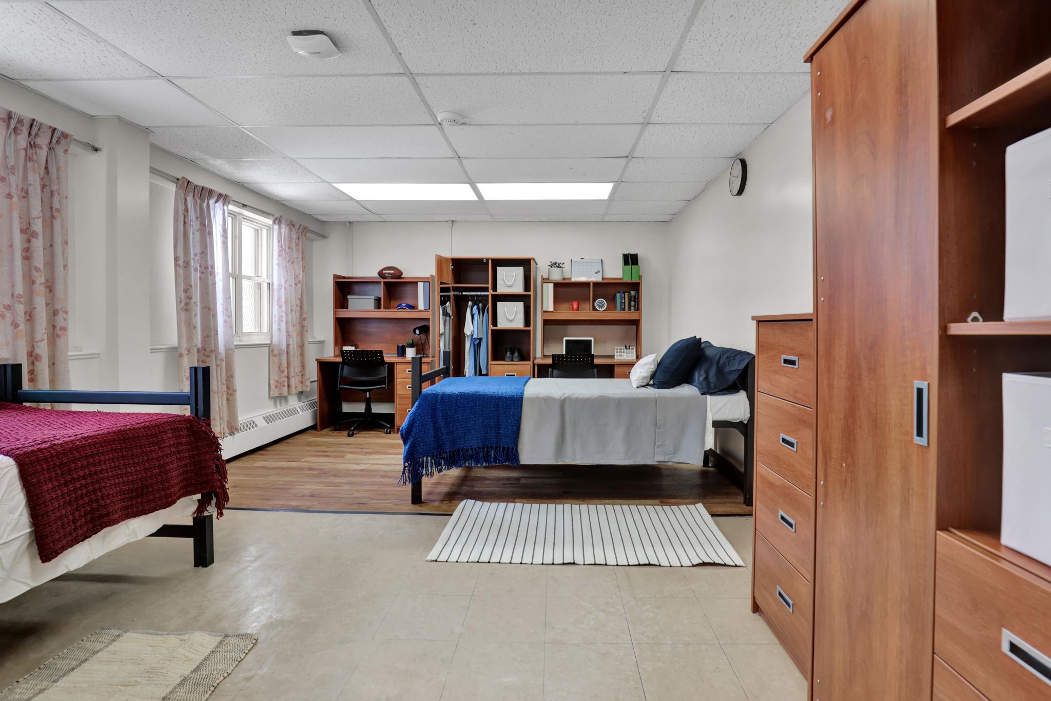 ​​A double room in Jean Royce Hall. Room features two beds, desks, and wardrobes. 