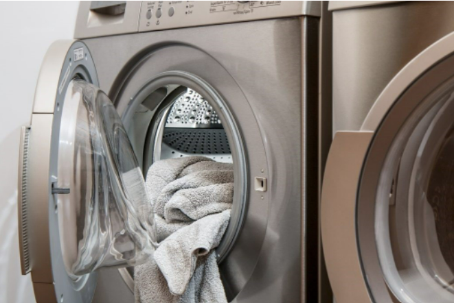 Front load washing machine with door open and towel hanging out. 
