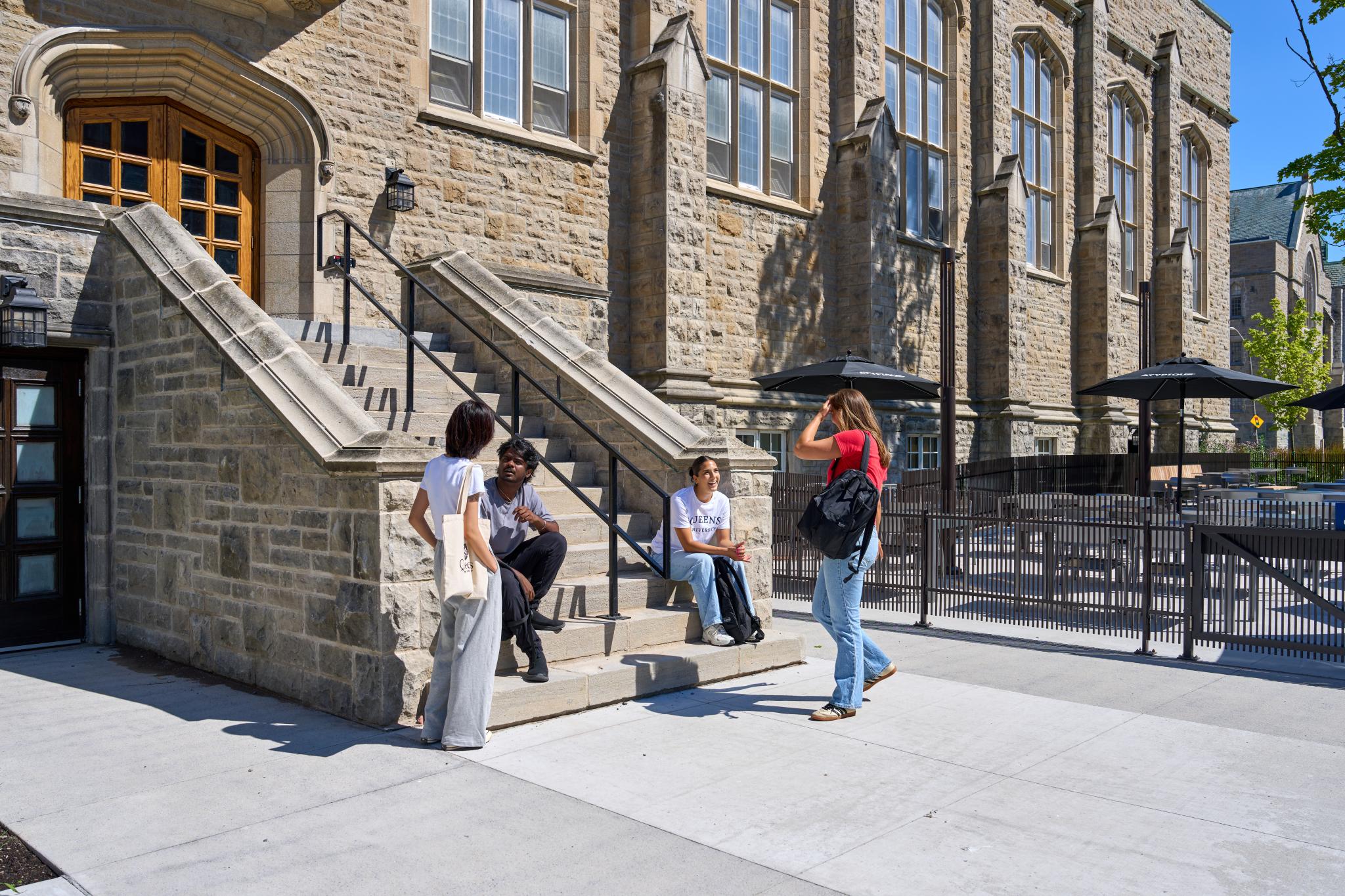 Four students chat by the steps at an entrance to the Jean Deutsch University Centre.