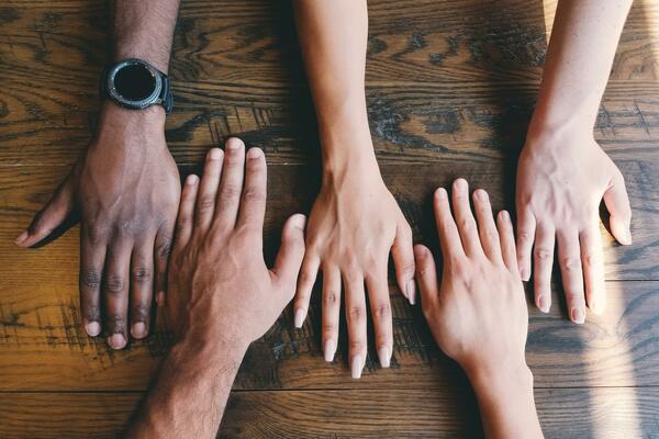 5 hands of different skin tones laying flat on a wooden surface