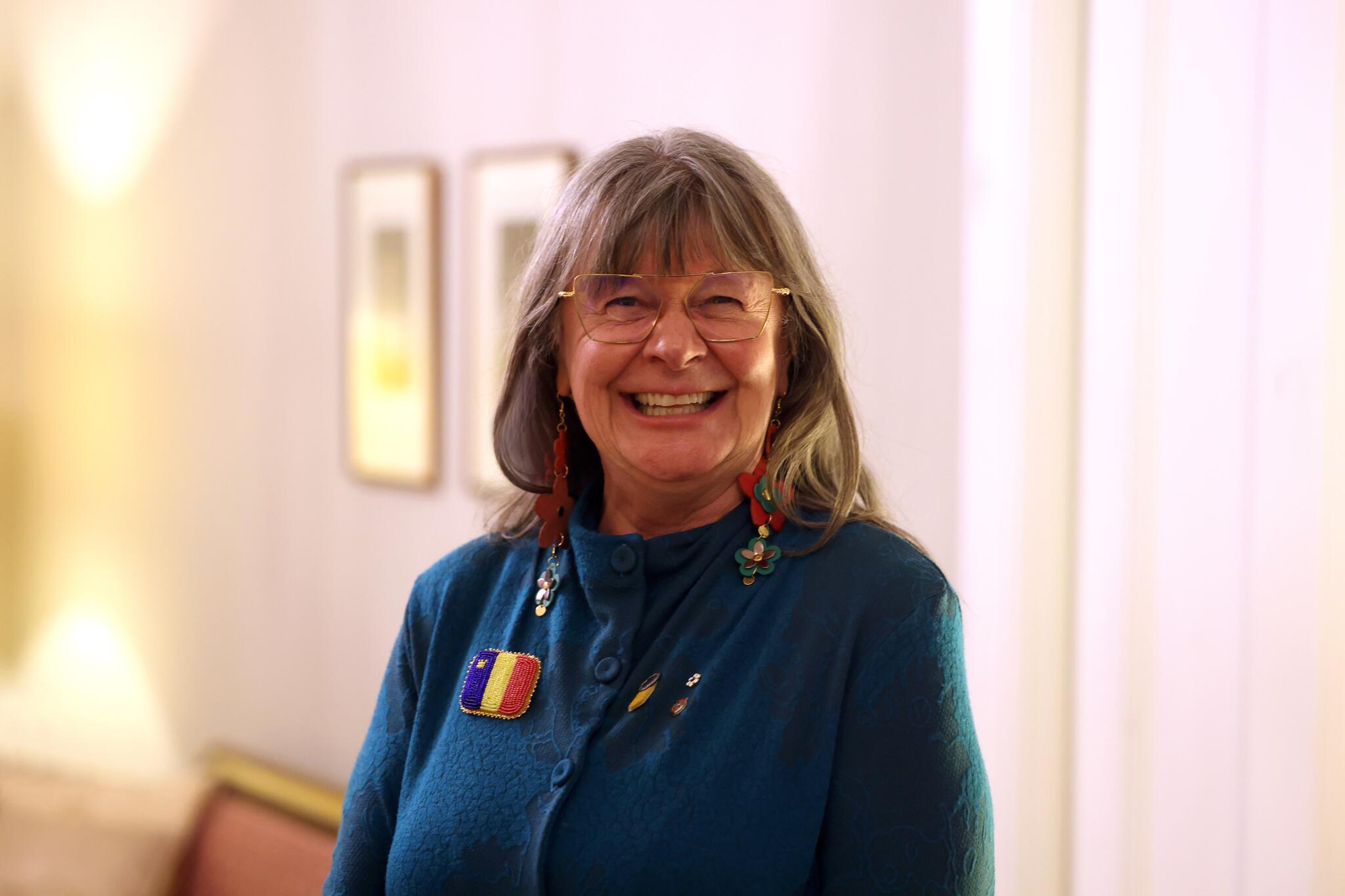 Women with grey brown hair and glasses in a blue top smiling