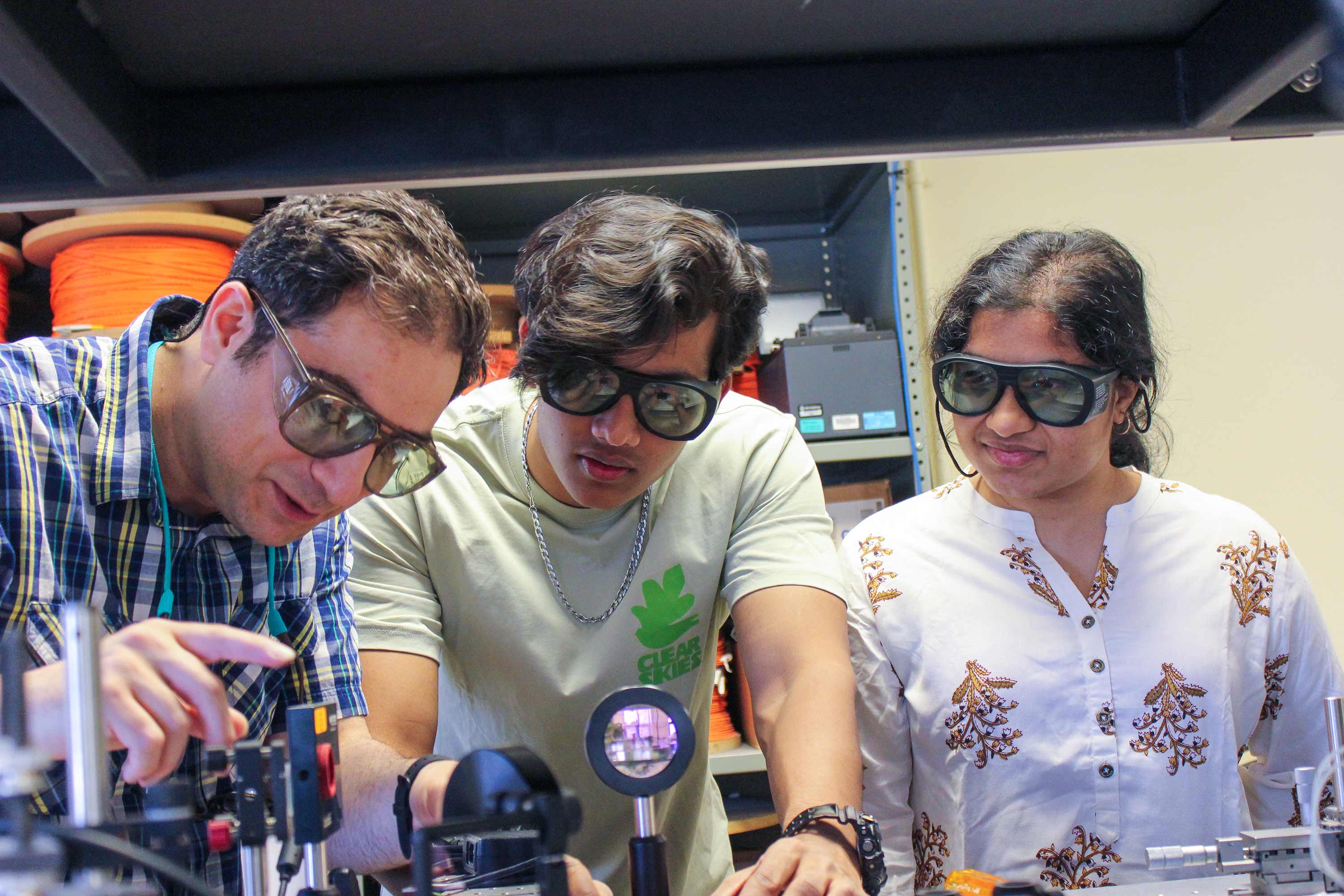 faculty and students wearing safety googles, looking at lab equipment 