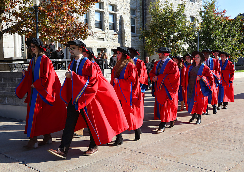 Group of graduate students at fall convocation walking in front of Grant Hall wearing red robes.