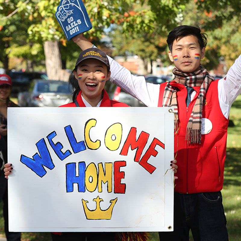 Queen's alumni holding welcome home sign at homecoming.