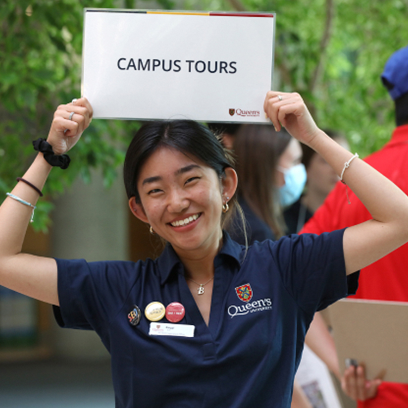 Smiling student holding a campus tours sign over head