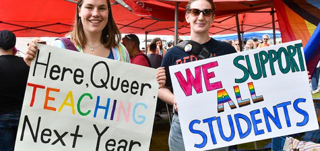 [Two Queen's staff hold pride posters at parade]