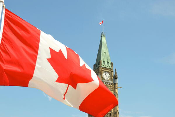 Canadian flag flying in front of Parliament buildings. 
