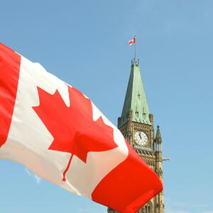 Canadian flag flying in front of Parliament buildings. 