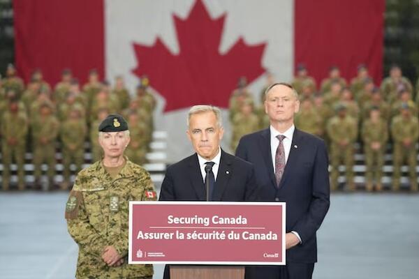 Prime Minister Carney stands in front of Canadian military and Canadian flag