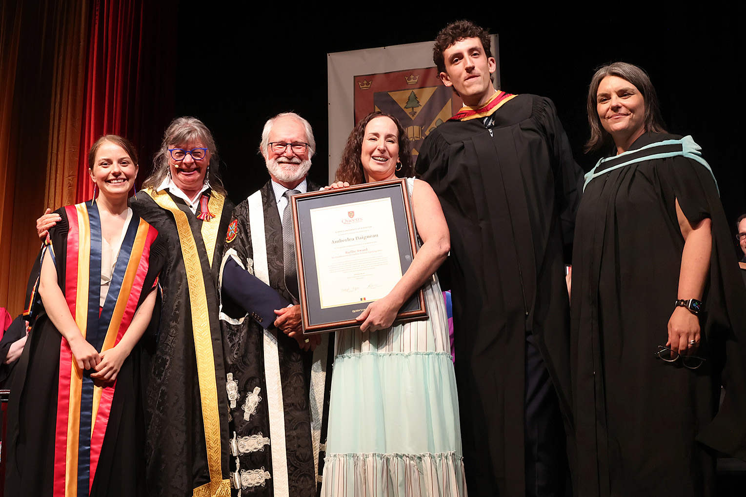 Baillie Award recipient Amberlea Daigneau on stage at the Spring 2025 convocation with (from left to right) Rector Niki Boytchuk-Hale, Chancellor Shelagh Rogers, Baillie Award nominator Blake Gill, Principal and Vice-Chancellor Patrick Deane, and Interim Vice-Provost & Dean of Student Affairs Corinna Fitzgerald.