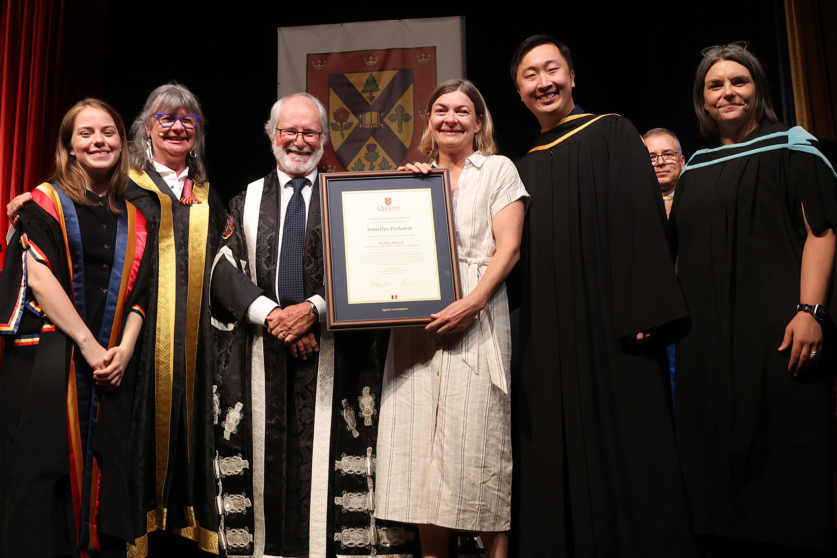 Baillie Award recipient Jennifer Petkovic on stage at the Spring 2025 convocation with (from left to right) Rector Niki Boytchuk-Hale, Chancellor Shelagh Rogers, Baillie Award nominator Kevin Liang, Principal and Vice-Chancellor Patrick Deane, and Interim Vice-Provost & Dean of Student Affairs Corinna Fitzgerald.