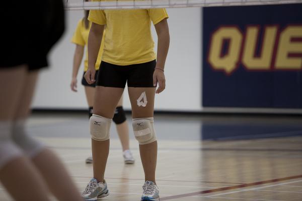 Three sets of legs under a volleyball net in the gym